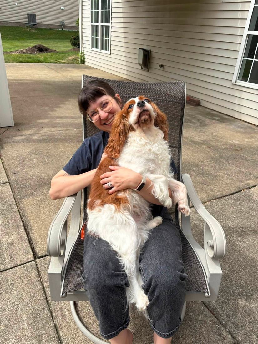 A sitter holding a happy Cavalier on the patio