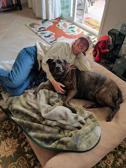 A sitter relaxing with a brindle dog on a dog bed