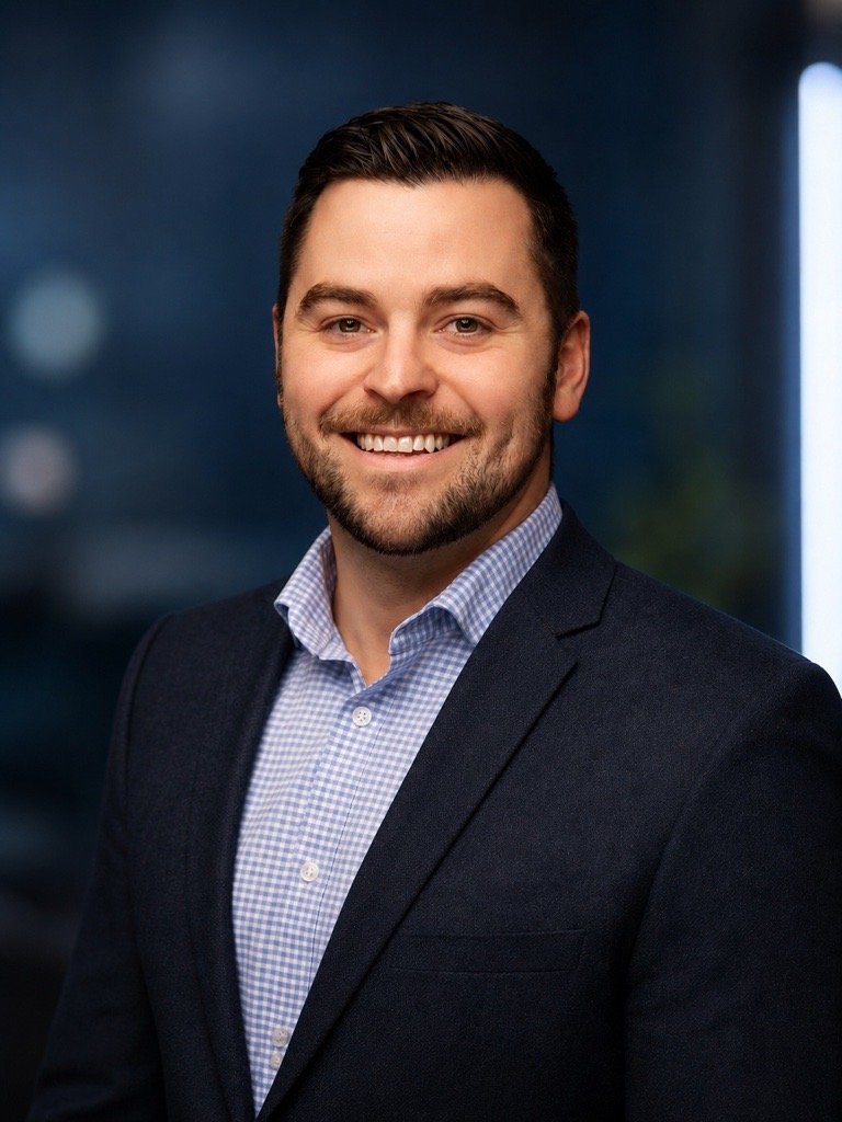 Jordan Yoerger in a navy blazer and checked shirt, smiling, against a blue studio background
