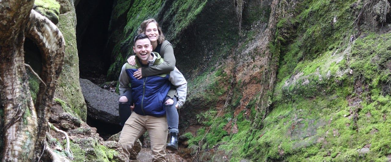 Jordan and a companion on a hike in front of a mossy rock face