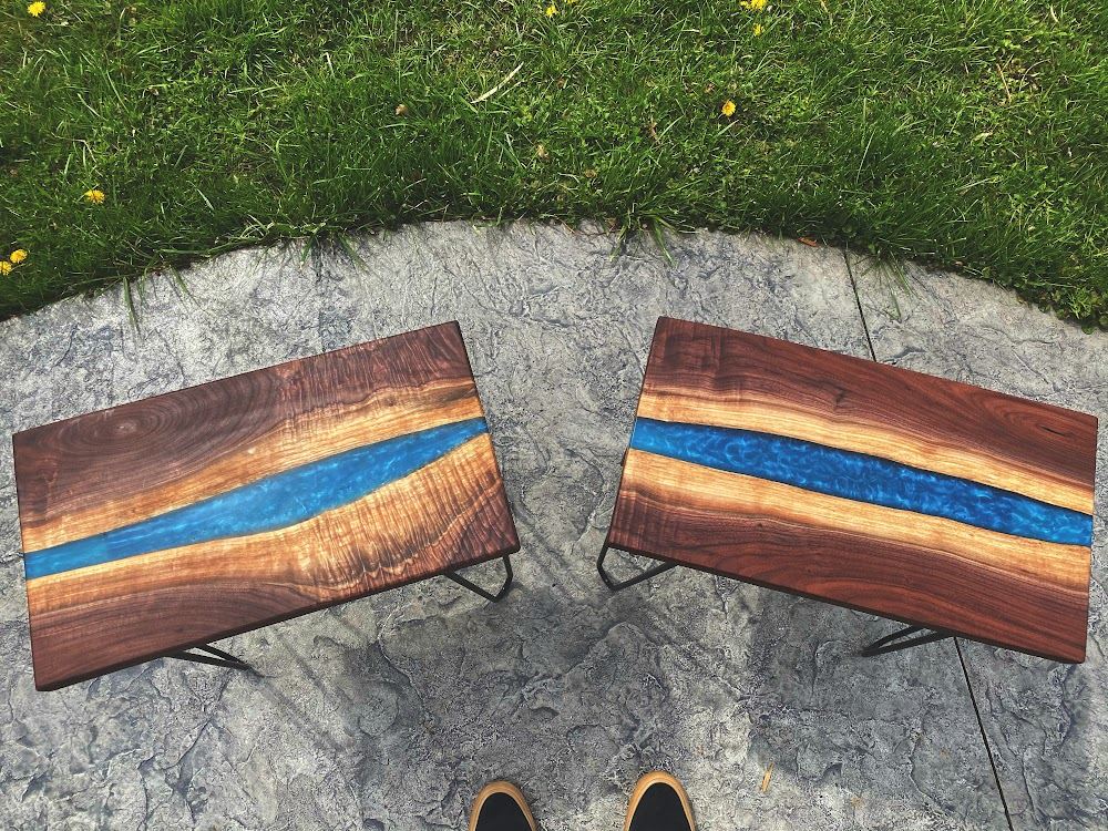 Two live-edge walnut coffee tables with blue epoxy rivers, standing on a lawn