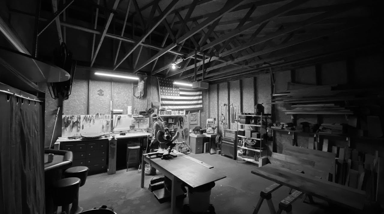The Yoergoods workshop in black and white: workbench, miter saw, lumber rack, and a flag on the wall